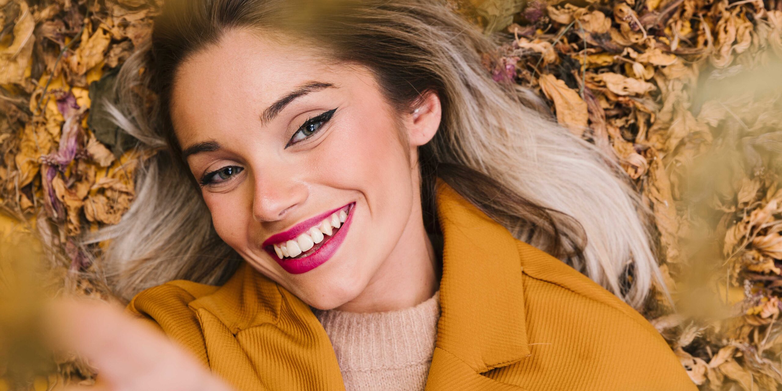 Femme souriant dans un tas de feuilles - Routine de maquillage pour l'automne